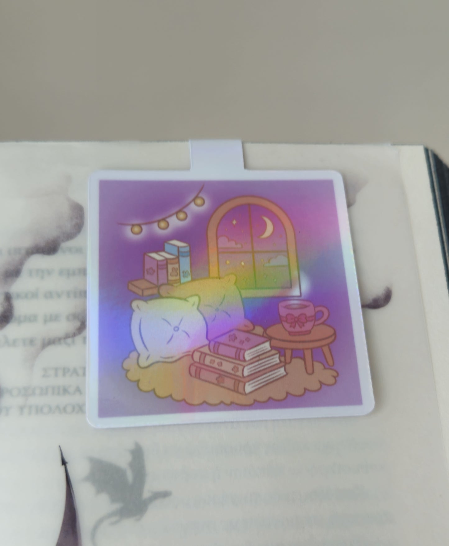 Holographic card with a cute illustration of a cat, books, and a cup on a table.