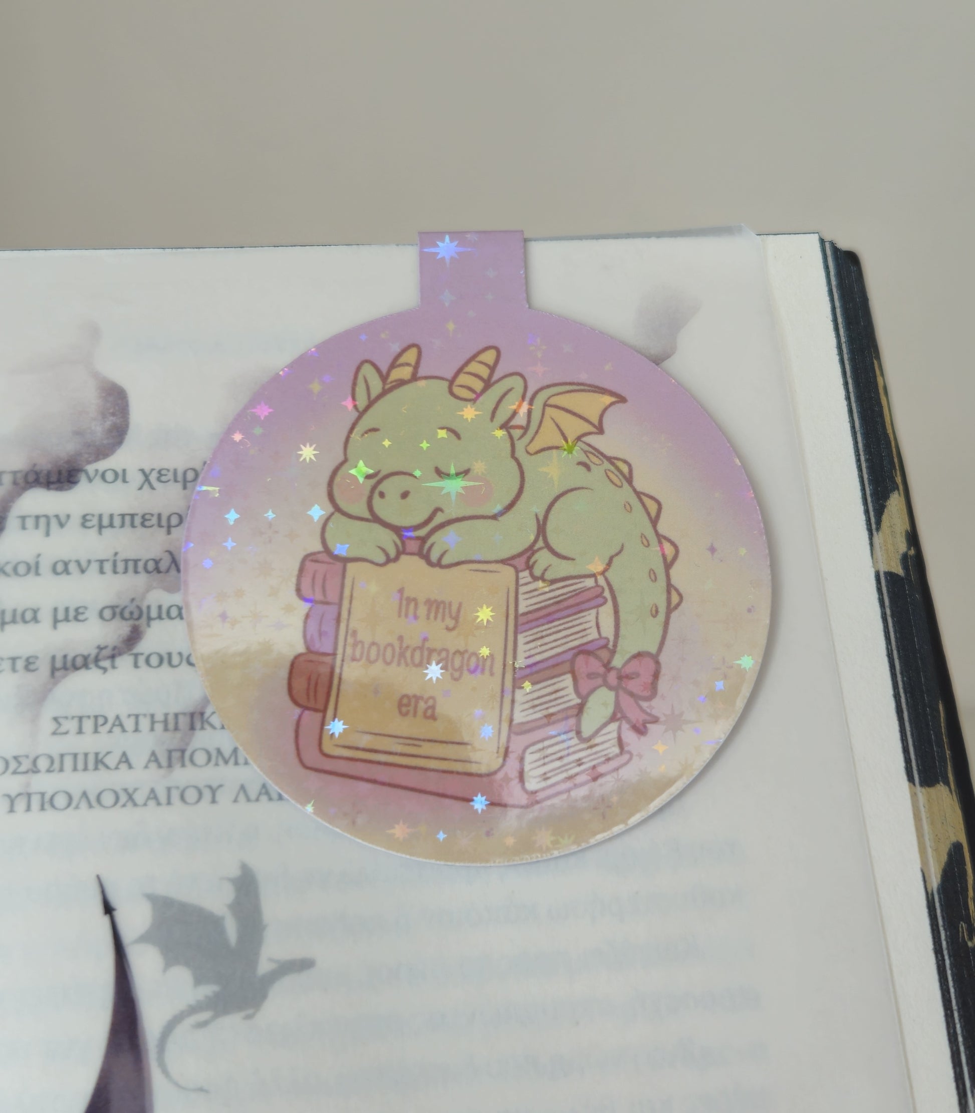 Decorative bookmark with a dragon holding a book on a white surface.